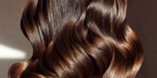 Cinematic close-up of sleek voluminous high-shine blowout hair in warm studio lighting representing the rich girl blowout luxury hair trend replacing beach waves in 2026