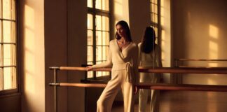 Balletcore Fashion Is Fueling a New Surge of Interest in Professional Ballet Model in wrap cardigan and satin ballet flats at a barre in a sunlit studio representing how the balletcore trend 2026 is inspiring adult ballet enrollment and luxury fashion