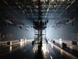Production crew setting up lighting rigs and staging inside a fashion week show venue, representing the behind the scenes costs of runway show production