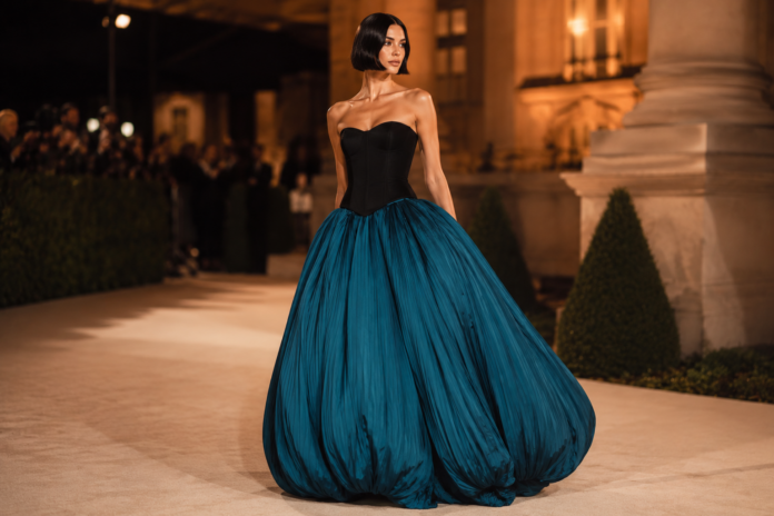 Chrissy Teigen wearing a strapless black corseted bodice and dramatic teal bubble skirt by Aisté Hong at the 2026 Gold Gala red carpet.