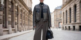Fashion week attendee in vintage racing jacket and tailored wide-leg trousers with luxury handbag on European street representing the Formula 1 fashion trend and motorcore street style aesthetic of 2026
