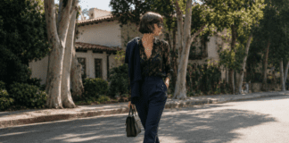 Kaia Gerber in a minimalist off-duty outfit featuring a black lacy blouse, navy tailored trousers, and black ballet flats on a Los Angeles street in 2026.