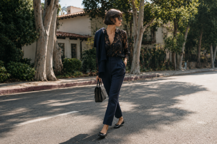 Kaia Gerber Minimalist Street Style — Model Off Duty 2026 Kaia Gerber in a minimalist off-duty outfit featuring a black lacy blouse, navy tailored trousers, and black ballet flats on a Los Angeles street in 2026.