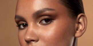 Latte Makeup Is Still Dominating—How Warm Bronze Tones Became 2026’s Most Wearable Glam Look Model wearing a latte makeup look with warm bronze eye shadow, cream bronzer on sun-kissed cheekbones, and a nude glossy lip against a warm champagne editorial background — illustrating the 2026 bronze makeup trend.