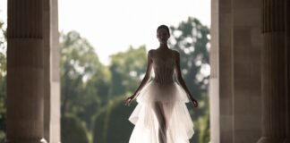 Maria Grazia Chiuri’s Nine Years at Dior Redefined What Romantic Femininity Means in Fashion Model in diaphanous ivory couture gown in a grand Parisian setting representing Maria Grazia Chiuri's nine-year Dior couture runway legacy and her redefinition of romantic femininity in French luxury fashion