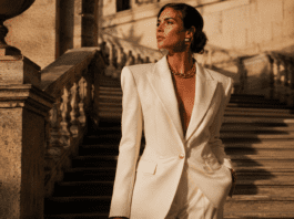 Model in a structured ivory wide-shoulder blazer with gold accessories on a sunlit stone staircase representing the new maximalism fashion trend in spring summer 2026