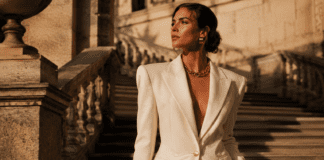 Model in a structured ivory wide-shoulder blazer with gold accessories on a sunlit stone staircase representing the new maximalism fashion trend in spring summer 2026