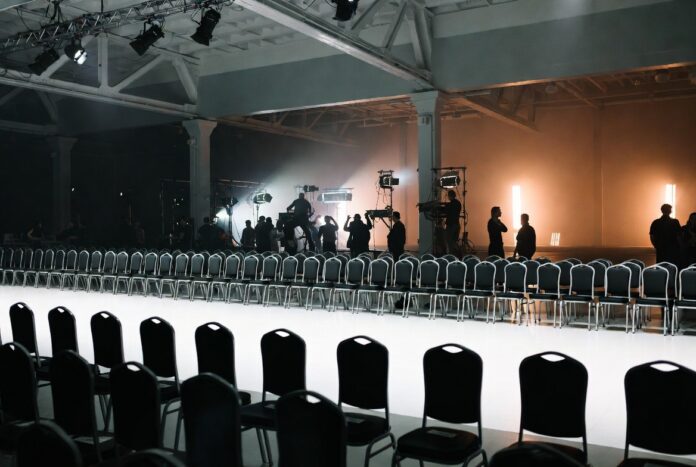 NYFW Schedule: How Shows Are Booked & Sequenced — Runway Magazine Empty New York Fashion Week runway with production crew preparing the venue before the show, illustrating how the NYFW schedule is built and sequenced