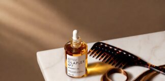 Olaplex No.7 Bonding Oil 30ml bottle on a white marble surface with a wide-tooth comb and glossy highlighted hair strand, editorial beauty product photography for a 2026 haircare review.