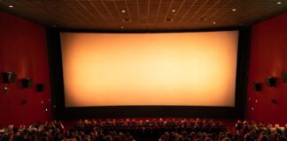 Summer Movie Season 2026 Is Shaping Up as Hollywood’s Biggest Comeback Year Wide shot of a packed premium movie theater auditorium with glowing screen light representing summer movies 2026 and Hollywood's biggest box office comeback season since the pandemic