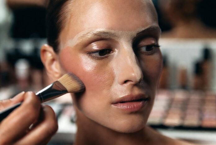 Underpainting Makeup Technique — Reverse Contouring for a Natural Finish Model's face mid-underpainting makeup application with cream contour blended along the cheekbone before a sheer foundation layer is applied, demonstrating the reverse contouring technique used by professional makeup artists.