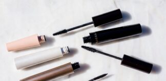 Editorial beauty flatlay of mascara tubes and open wands arranged on white marble representing the best mascara 2026 comparison between viral TikTok drugstore formulas and luxury clean beauty brands